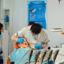 stomatologist-talking-with-mother-kids-lighting-lamp-examining-little-girl-standing-near-stomatological-chair-pediatric-dentist-speaking-woman-while-nurse-preparing-sterilized-tools_482257-13331